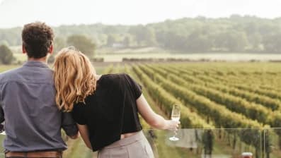 A couple walking through the vineyard with glasses of wine in hand